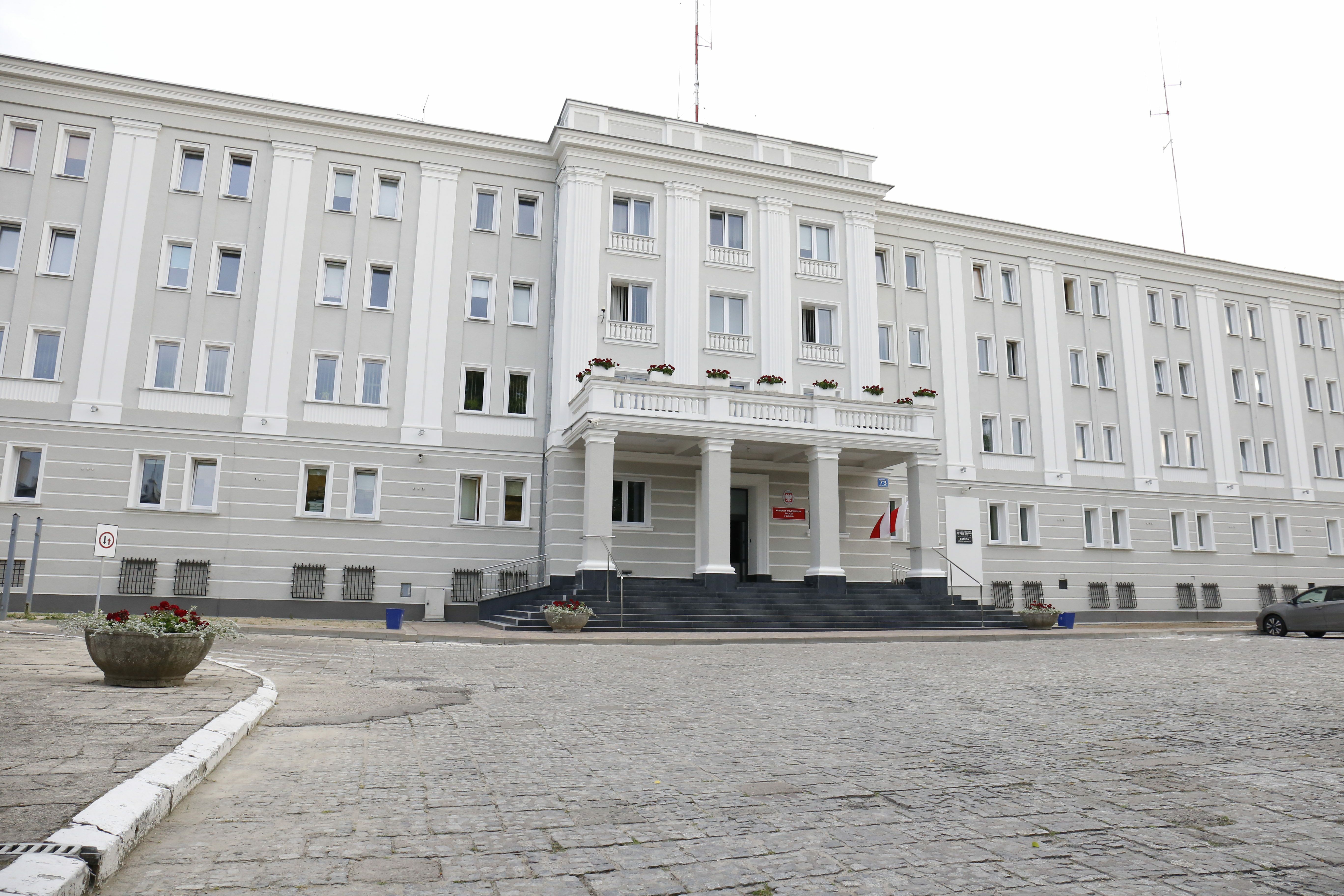 Zdjęcie przedstawia siedzibę Komendy Wojewódzkiej Policji w Lublinie. W kadrze widoczny jest trzypiętrowy budynek w kolorze biało-szarym. Zdjęcie przedstawia wejście główne do budynku, zlokalizowane od strony ulicy Narutowicza.  